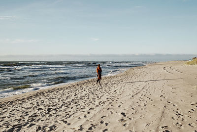 Rear view of woman on beach against sky