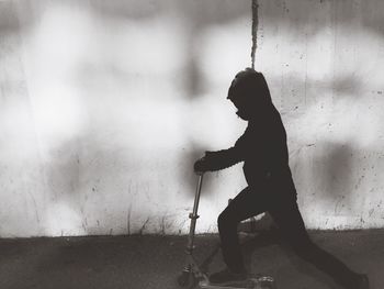 Side view of child in costume riding push scooter on road against wall