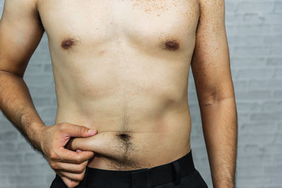 Midsection of shirtless man touching stomach against wall