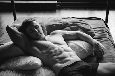 High angle view of shirtless muscular male model lying on bed at home