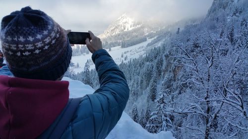 Rear view of man photographing mountains during winter using smart phone