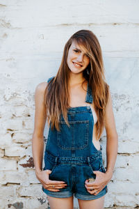 Portrait of smiling young woman standing against wall