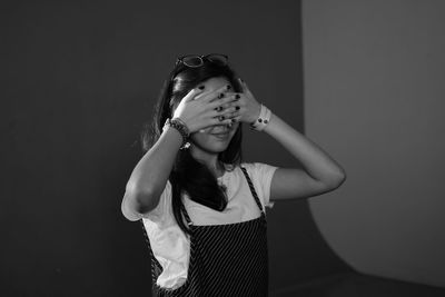 Young woman covering face with hands while standing against wall