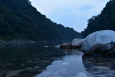 Rocks by river against sky