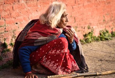 Senior woman crouching against brick wall