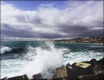 Waves splashing on rocks against cloudy sky