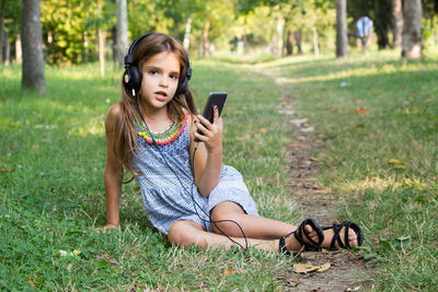 Full length of girl using mobile phone sitting at park