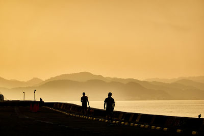 Silhouette people standing by the sea against sky during sunrise