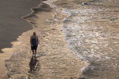 Adult man walking on a beach with ocean wave during sunrise