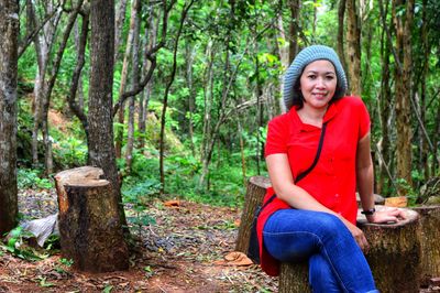 Portrait of smiling woman sitting on tree trunk in forest