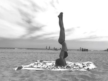 Woman doing handstand at beach against sky