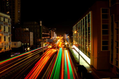 Light trails on road by illuminated buildings at night