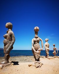 Statues at beach by sea against clear blue sky