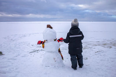 Boy sits alone with snowman and looks forward. loneliness and friend made of snow. winter mood