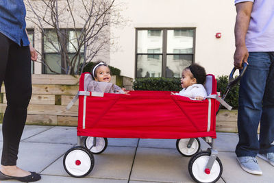 Low section of parents standing by daughters sitting in baby carriage on footpath