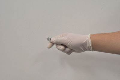 Close-up of hand holding cigarette against white background