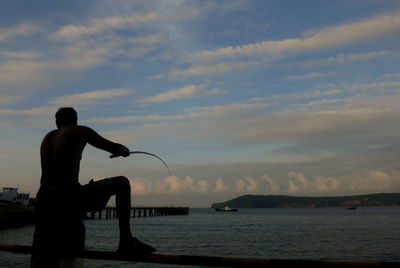 Silhouette man standing by sea against sky during sunset