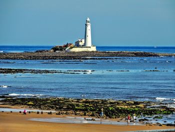 Lighthouse by sea against clear sky