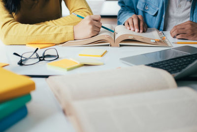 Midsection of friends reading book while sitting at table