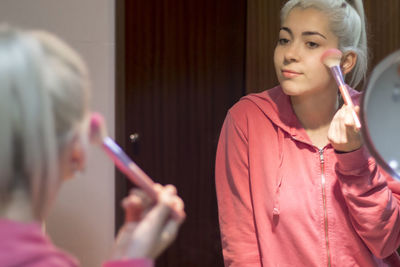 Smiling young woman applying make up in bathroom