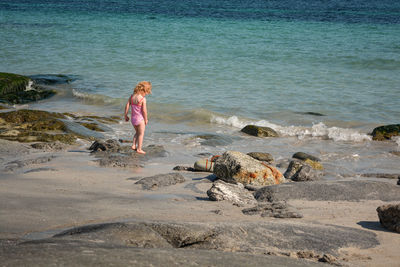 Rear view of girl standing on rock at beach