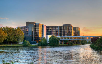 River by buildings against sky during sunset