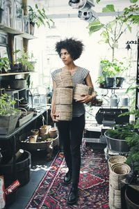 Full length of woman carrying wicker pots in interior design shop