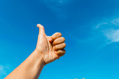 Cropped hand gesturing thumbs up against blue sky