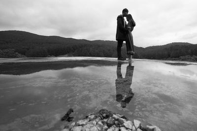 Rear view of man standing by lake against sky