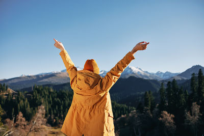 Rear view of woman with arms raised standing on mountain against clear sky