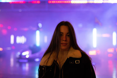 Portrait of young woman standing against illuminated light at night