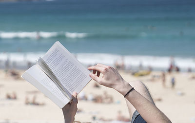 Low angle view of hand holding book at beach