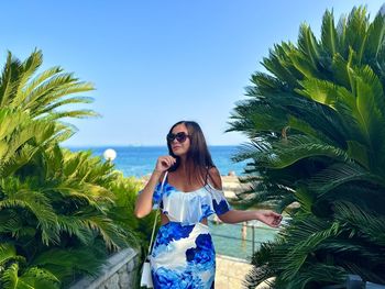 Young woman standing against palm trees