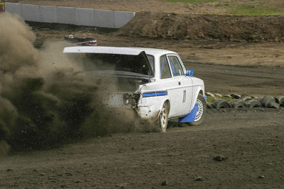 Rally car driving with a open trunk and a gravel dust behind him