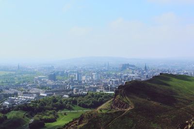 Scenic view of holyrood park by cityscape against sky