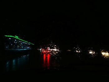 Illuminated city by river against sky at night