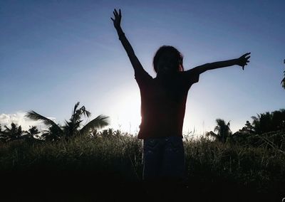 Woman with arms raised standing on field against clear sky