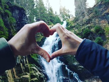 Cropped hands of couple making heart shape against waterfall