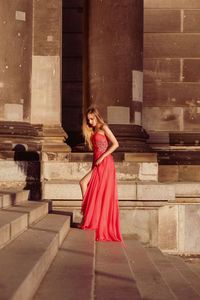 Full length side view of young woman in pink evening gown standing at on steps