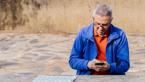 Senior man looking and touching screen of smartphone while sitting on park