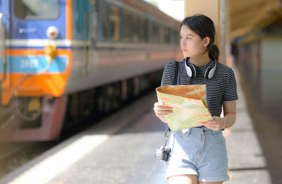 A young european girl traveler holding a map standing on the train platform.