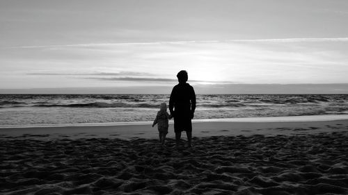 Silhouette father and child walking on shore at beach