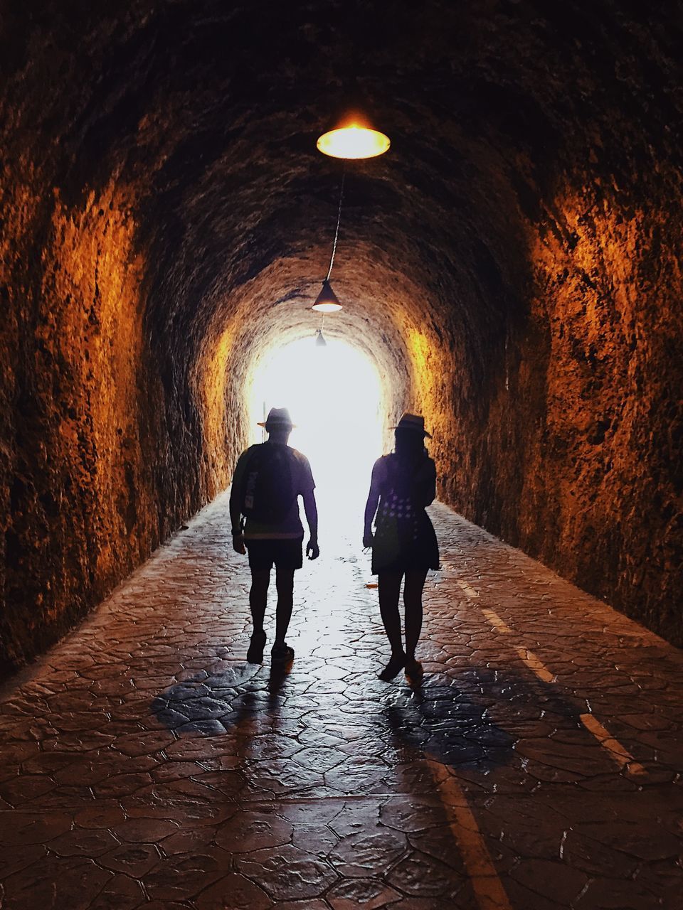 FULL LENGTH REAR VIEW OF PEOPLE WALKING ON ILLUMINATED TUNNEL