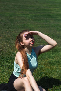 Portrait of woman shielding eyes while sitting in park