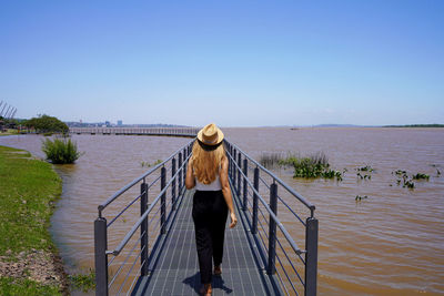 Rear view of woman walking on pier over sea against clear sky