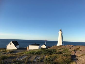 Lighthouse by sea against clear blue sky