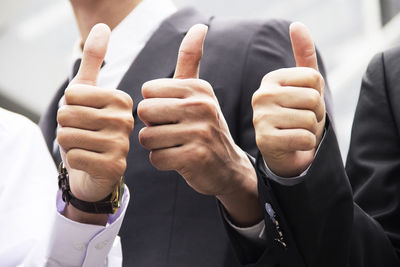 Midsection of business people showing thumbs up while standing outdoors