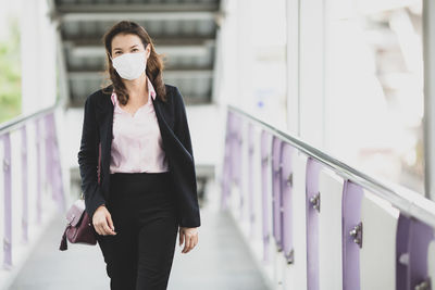 Portrait of businesswoman wearing mask walking on footbridge
