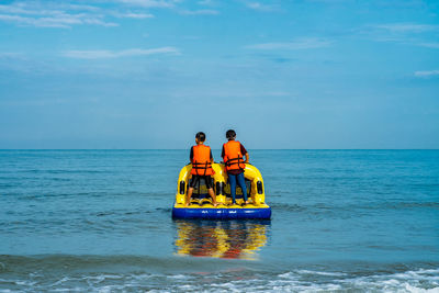 Rear view of boys standing on inflatable raft in sea against sky