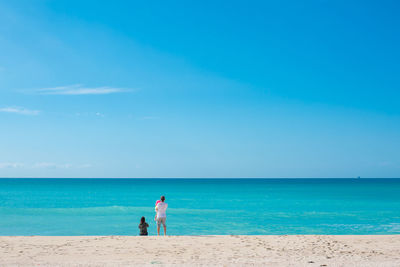 People on calm beach against blue sky